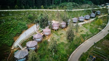 A series of dome-shaped cabins arranged in a row along a curved road, surrounded by dense greenery and a forested backdrop.