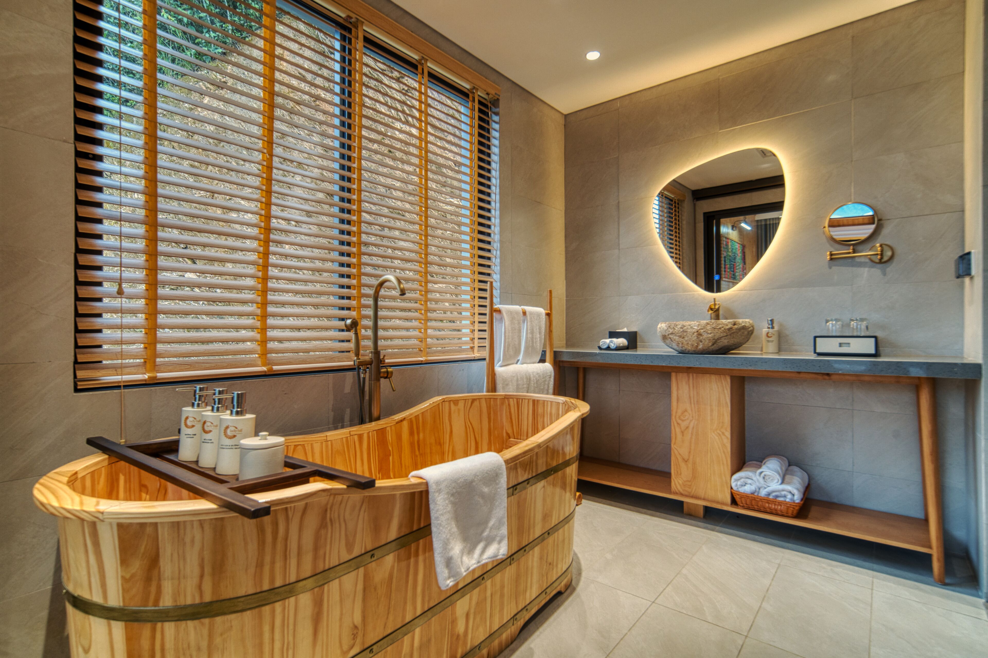 Un baño moderno con una bañera de madera, un espejo grande y una ventana con persianas.