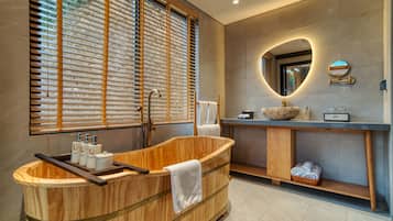 Un baño moderno con una bañera de madera, un espejo grande y una ventana con persianas.