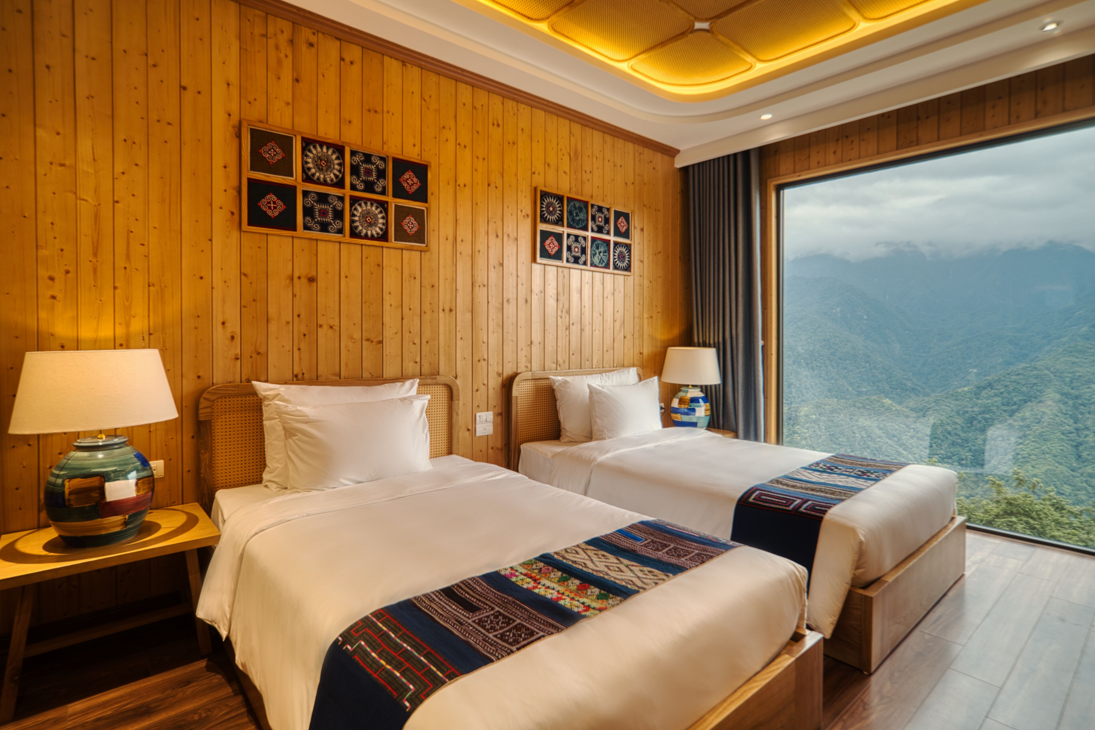 A hotel room with two beds, wooden paneling, and a large window offering a mountain view.