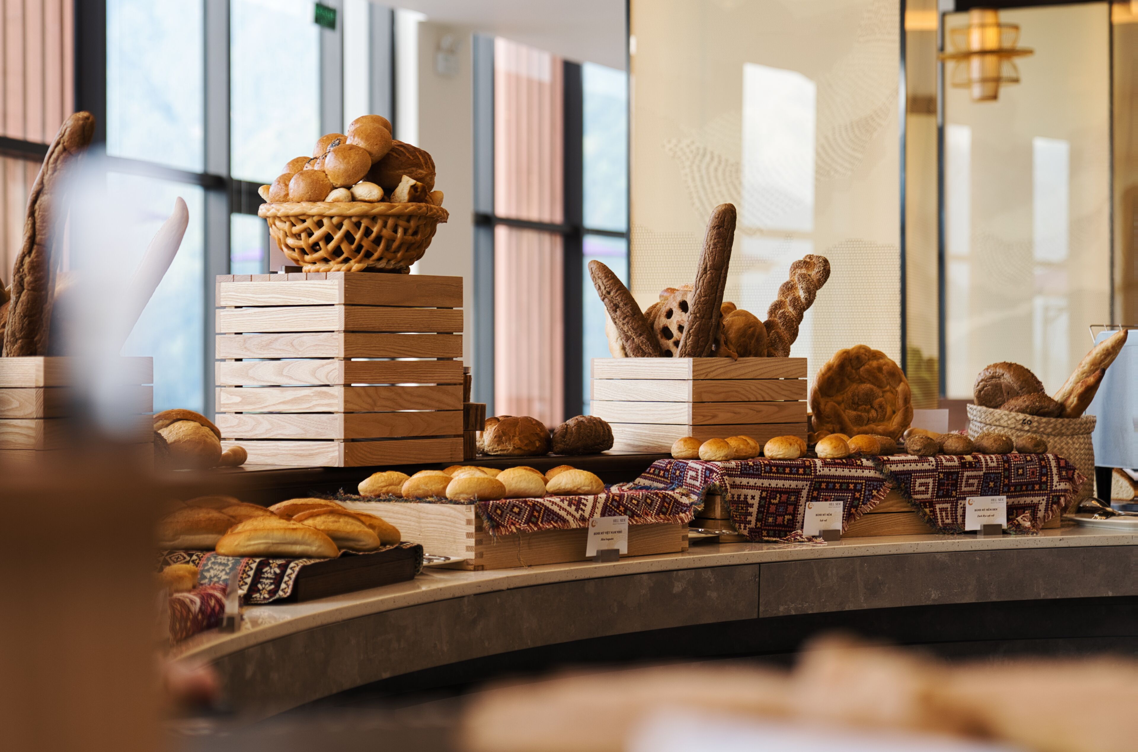 A bakery display with various breads and pastries, including loaves and rolls, arranged on wooden shelves and baskets.