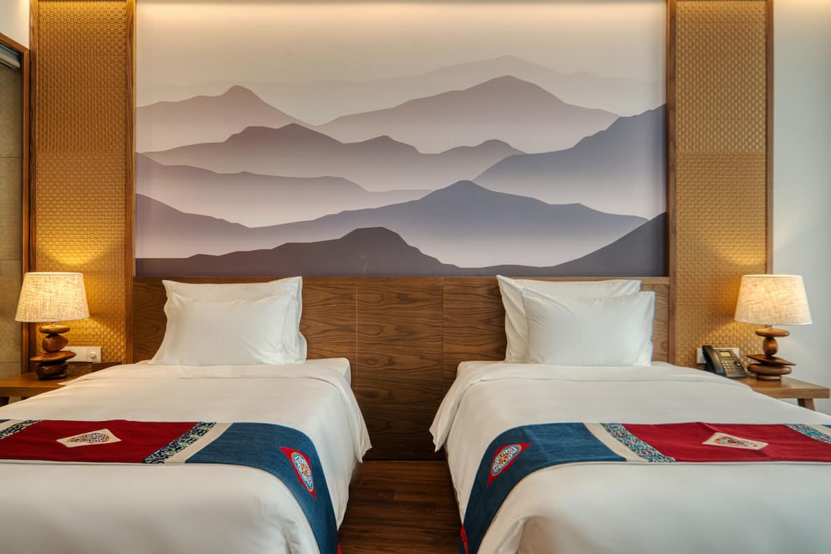 Ein Hotelzimmer mit zwei Betten, einem großen Wandbild von Bergen und zwei Nachttischlampen.