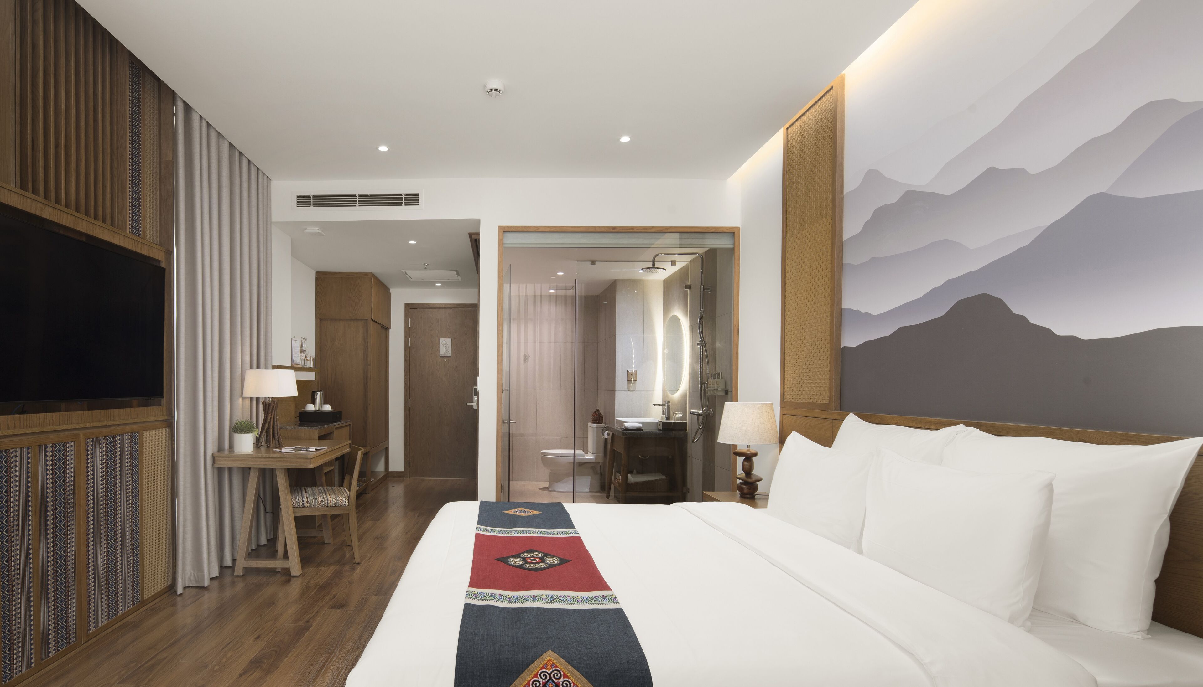 Una habitación de hotel con una cama grande, un escritorio con silla, un televisor y un baño con ducha.