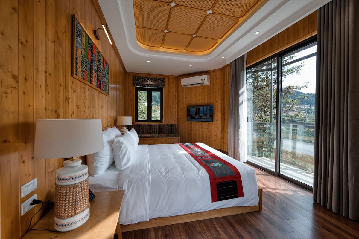 Ein geräumiges Schlafzimmer mit einem großen Bett, Holzwänden, einer Deckenleuchte und einem großen Fenster mit Blick ins Freie.