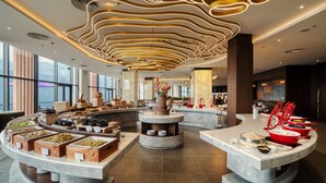 Een moderne hotel lobby met een centraal eiland waarop verschillende eetmogelijkheden en een uniek plafond staan.