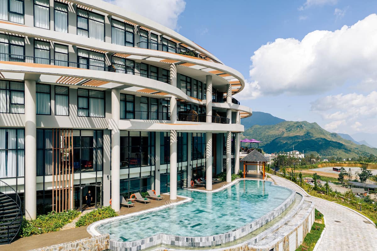 Ein modernes Hotel mit großem Pool, mehreren Balkonen und Bergblick.
