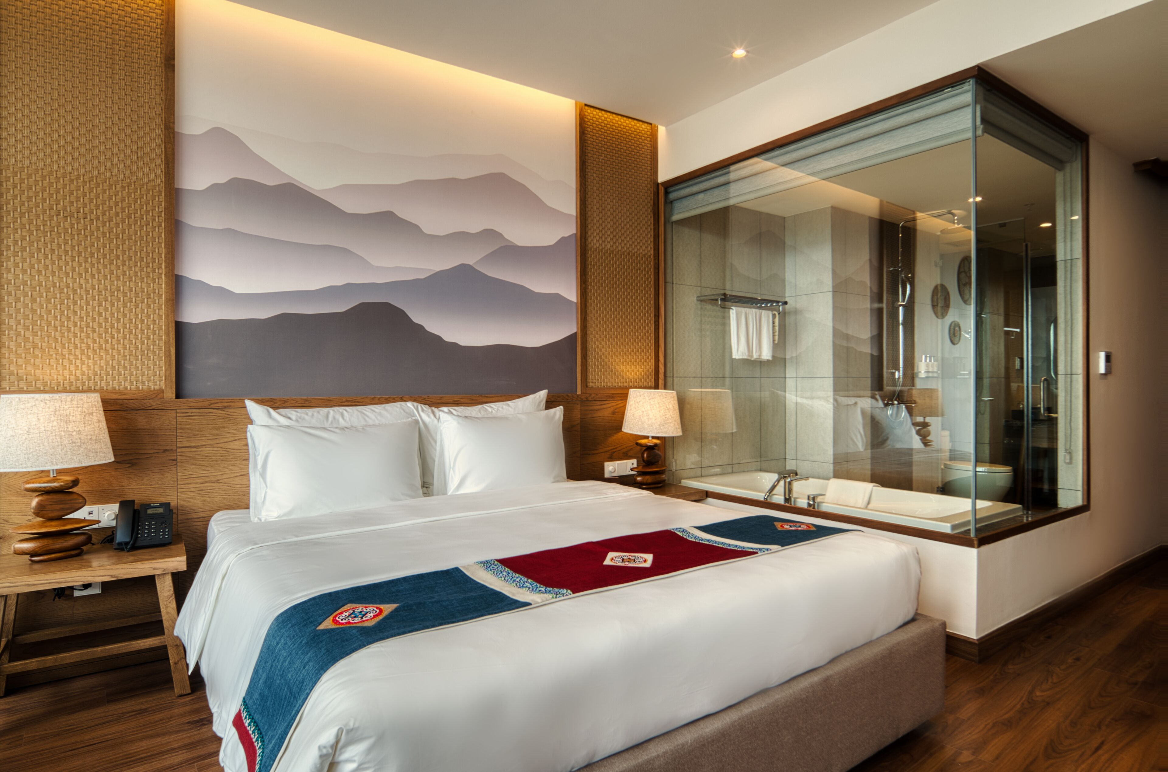 Una habitación de hotel con una cama grande, ducha con cerramiento de vidrio y un mural en la pared.