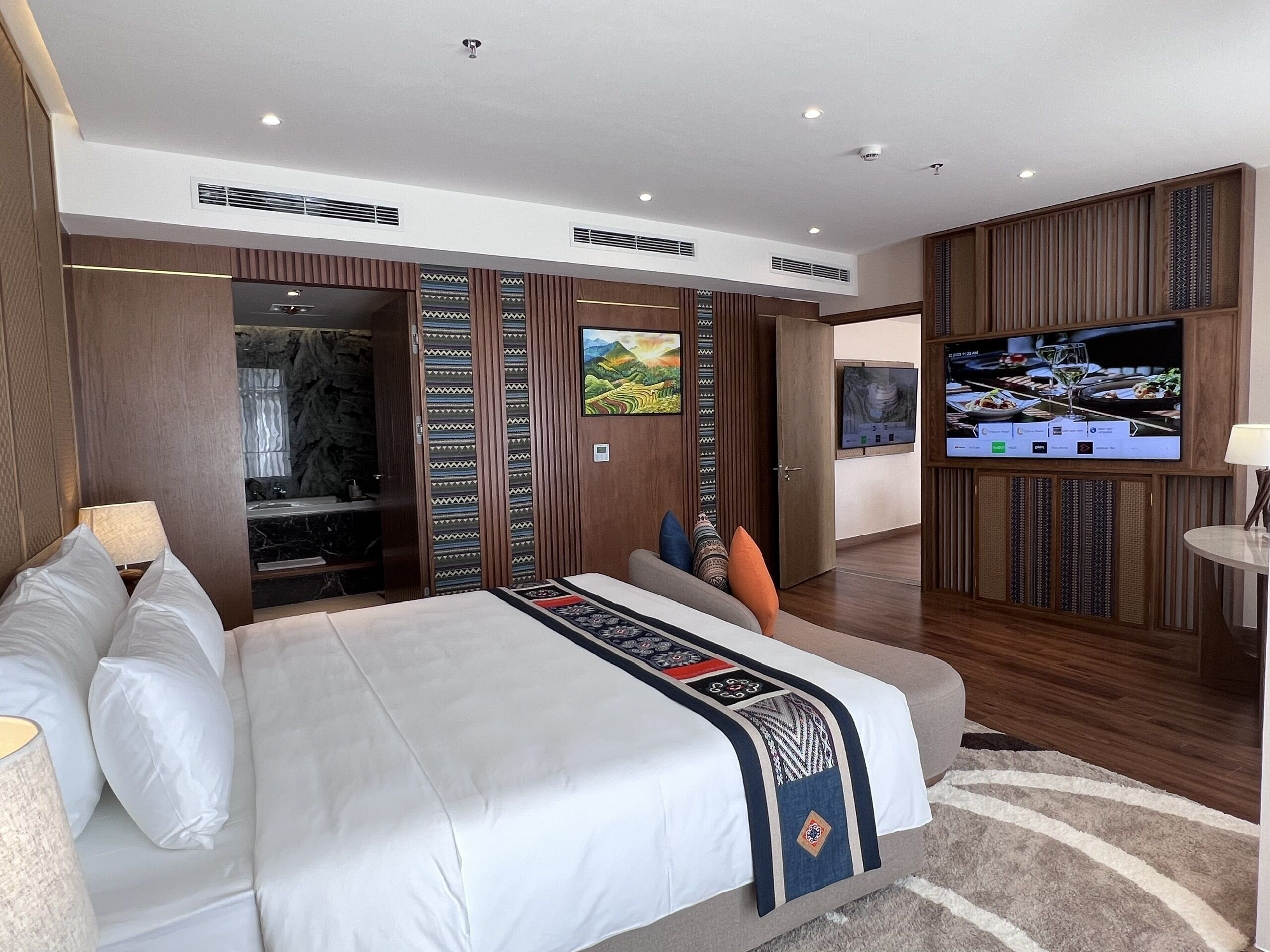 Een moderne hotelkamer met een groot bed, een televisie, een badkamer met een marmeren wastafel en een wand van hout.
