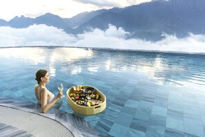 A person in a pool with a floating basket of food and drink, surrounded by mountains and clouds. - Lady Hill Sapa Resort (Sa Pa)