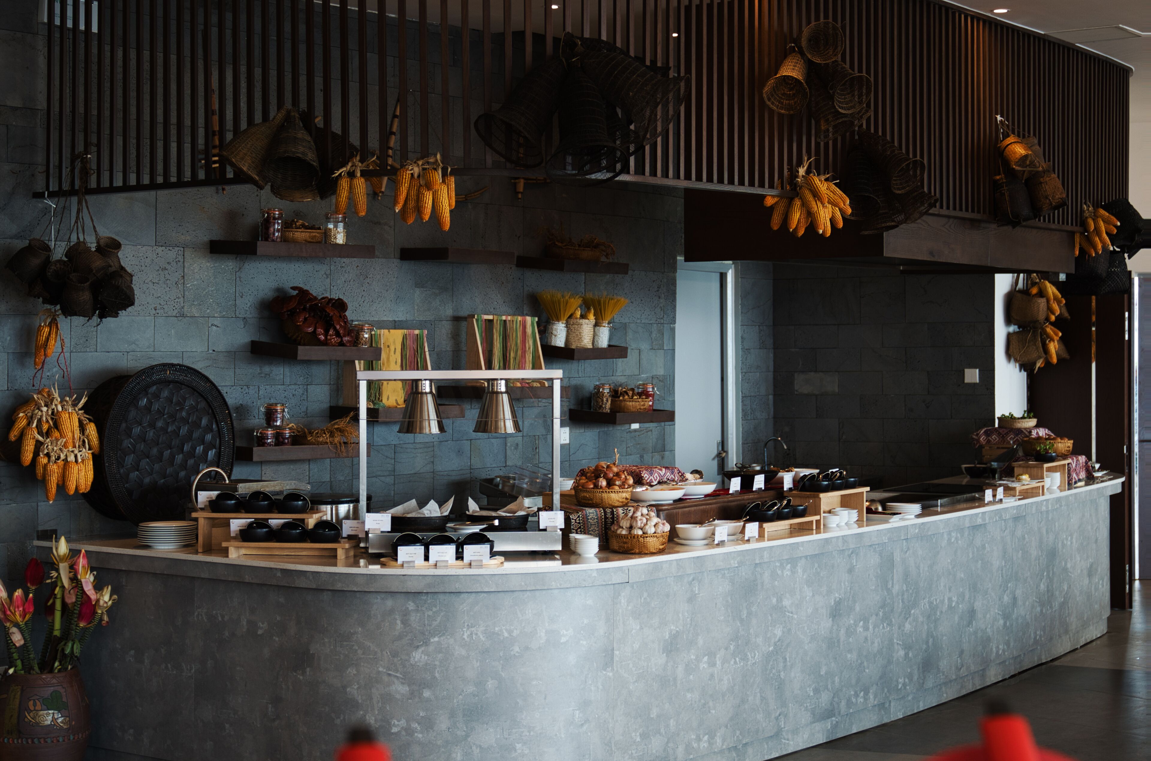A modern kitchen with a central island, various cooking utensils, and hanging baskets of produce.