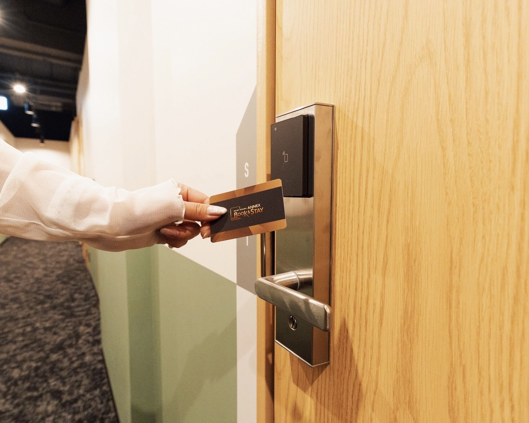 A hand inserting a card into a modern door lock labeled "Book & Stay".