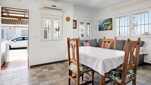 A dining area with a table and chairs, a sofa, a painting, and a view of the outside.