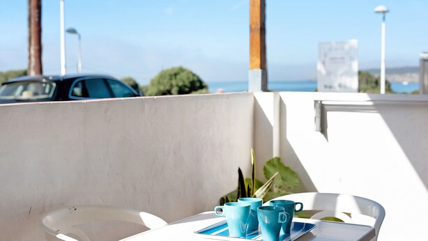 A table with a tray, a chair, and a view of the sea and a car in the background.