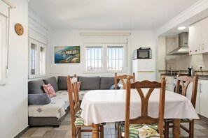 Ein Essbereich mit Tisch und Stühlen, eine Sitzecke mit Kissen, ein Bild an der Wand und eine Küche im Hintergrund.