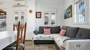 A room with a dining table, a sofa, a window with a view, and a clock on the wall.