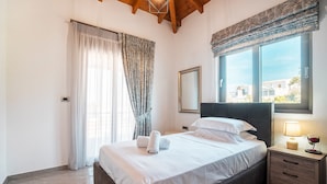 A bedroom with a bed, curtains, a bedside table with a lamp, and a window with a view.