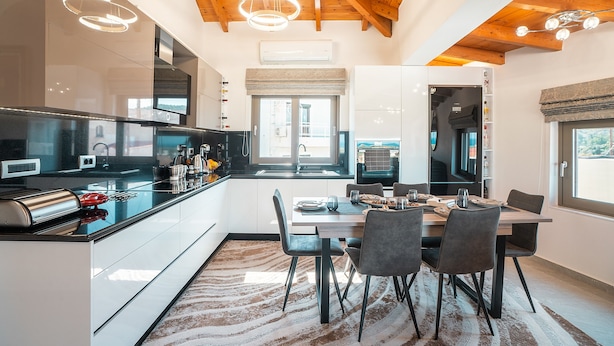 A modern kitchen with a dining area, wooden ceiling beams, and a large window.