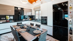 A modern kitchen with a dining area, wooden ceiling beams, and a view of the outdoors.