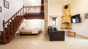 A bedroom with a bed, a wooden staircase, a living area with a sofa, a fireplace, and a TV. - Villa 'Nikolaos' with Sea View, Wi-Fi and Air Conditioning (Rhodes)
