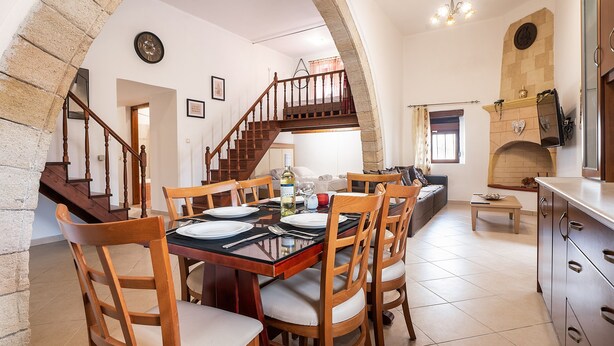 A dining area with a wooden table set for four, a staircase, and a stone fireplace. - Villa 'Nikolaos' with Sea View, Wi-Fi and Air Conditioning (Rhodes)