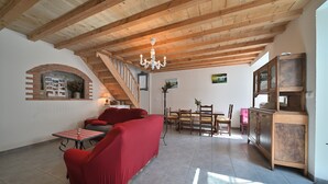 Un amplio salón con un sofá rojo, una mesa de comedor de madera y una escalera que sube a un nivel superior.