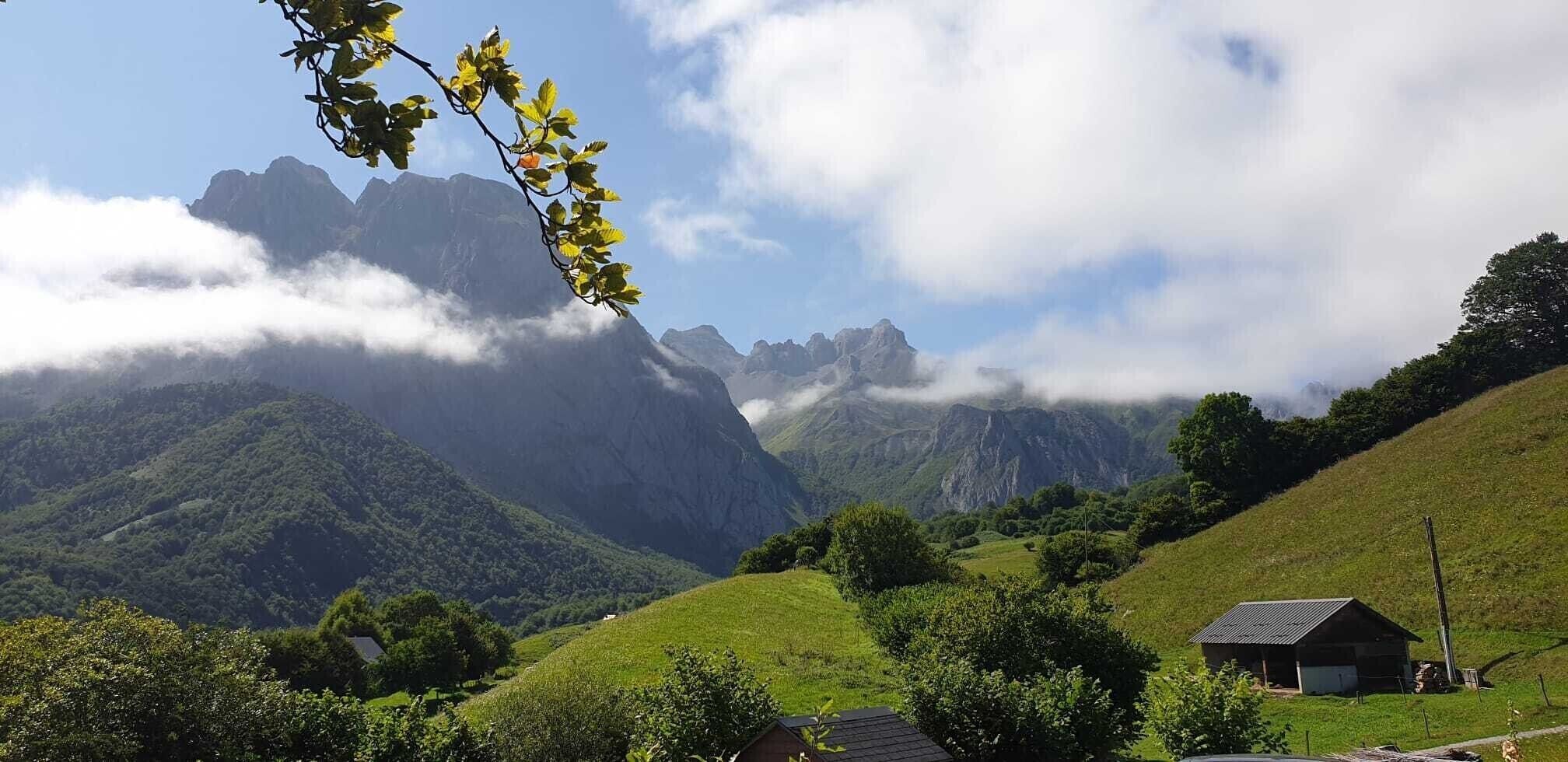 A mountainous landscape with a small building, lush greenery, and a clear sky.