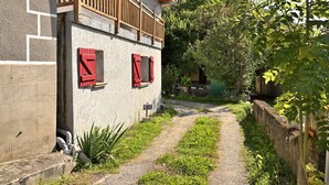 Un estrecho sendero que lleva a un edificio con balcón de madera y contraventanas rojas.