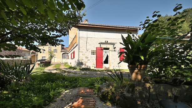 Un edificio con fachada de piedra, puerta roja y un jardín con senderos de grava y plantas.