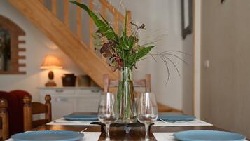 A dining table with blue placemats, clear glassware, and a vase with green and purple foliage.
