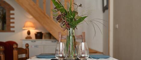A dining table with blue placemats, clear glassware, and a vase with green and purple foliage.