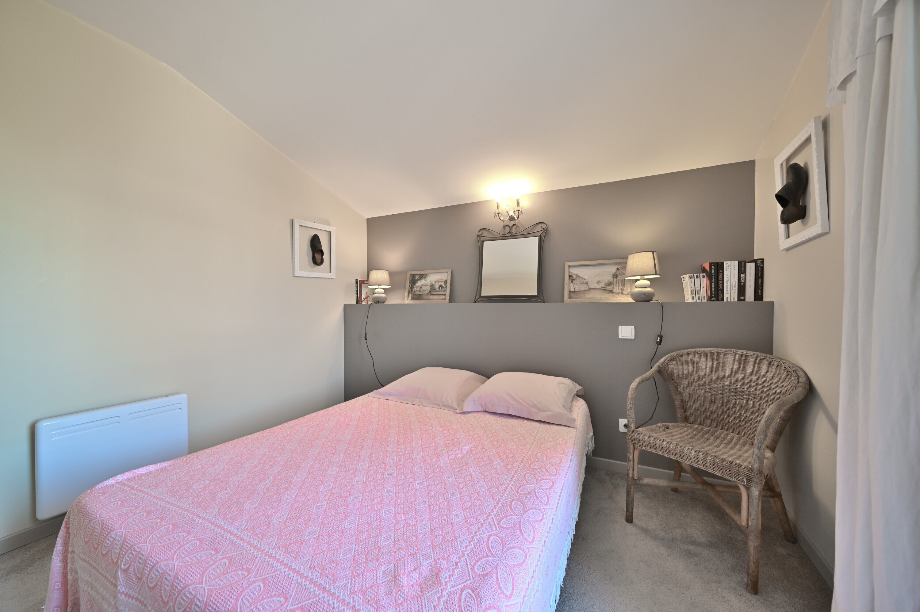 Ein Schlafzimmer mit Bett, Sessel, Wandspiegel und Heizkörper.