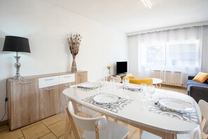 Ein modernes Wohnzimmer mit Esstisch für vier Personen, einer Couch, einem Fernseher und einem Fenster mit Vorhängen.