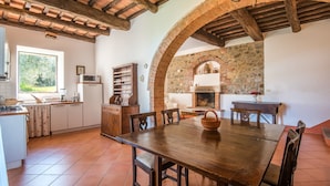 A rustic kitchen with a wooden table, chairs, and a brick fireplace.