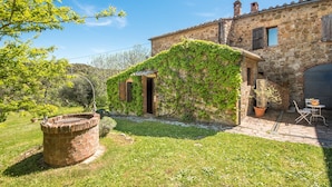 A stone building with ivy-covered walls, a brick well, and a patio with outdoor furniture.