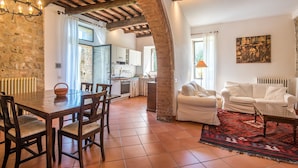 A spacious living area with a dining table, white sofas, and a kitchen in the background.