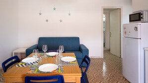 A dining area with a table set for two, a blue sofa, a white refrigerator, and a patterned floor. - Holiday Home 'A Due Passi dal Mare' with Sea View, Wi-Fi and Air Conditioning (Porto Cesareo)