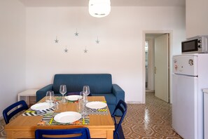 Un coin repas avec une table dressée pour deux personnes, un canapé bleu, un réfrigérateur blanc et un sol à motifs.