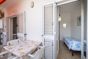Une pièce avec une table et des chaises, un lit recouvert d’une couverture bleue et une fenêtre offrant une vue circulaire.