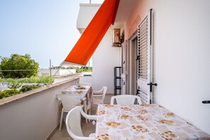 Un balcon avec une table et des chaises, un auvent rouge et une fenêtre avec des stores.