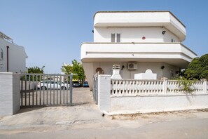 A multi-story building with a gated entrance, a car parked in the driveway, and a clear sky. - Holiday Home 'A Due Passi dal Mare' with Sea View, Wi-Fi and Air Conditioning (Porto Cesareo)
