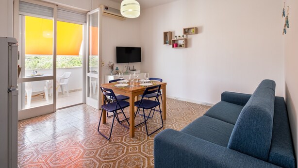 A room with a dining table, chairs, a sofa, a TV, and a patterned floor. - Holiday Home 'A Due Passi dal Mare' with Sea View, Wi-Fi and Air Conditioning (Porto Cesareo)