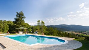 Una piscina con un pabellón, sillas de descanso y vistas a las montañas.