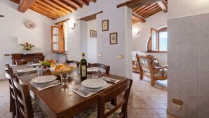 Un comedor con una mesa de madera dispuesta para cuatro, sillas, un jarrón con flores y vistas a la cocina y la sala de estar.
