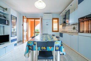 A dining area with a table set for four, a television on a stand, and a kitchen area with cabinets and a microwave. - Apartment "Residenza del Sole 1" with Shared Pool & A/C (Villasimius)