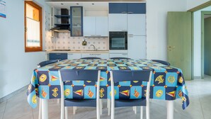 A compact kitchen with white cabinets, a built-in oven, and a dining table with a nautical-themed tablecloth. - Apartment "Residenza del Sole 1" with Shared Pool & A/C (Villasimius)