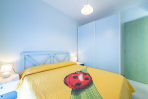 A bedroom with a bed, a nightstand, a lamp, and a door. - Apartment "Residenza del Sole 1" with Shared Pool & A/C (Villasimius)