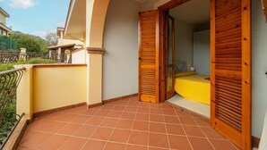A balcony with a tiled floor, wooden shutters, and a yellow bed. - Apartment "Residenza del Sole 1" with Shared Pool & A/C (Villasimius)