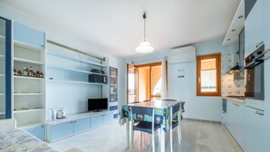 A compact kitchen with a dining table, built-in shelves, and a television. - Apartment "Residenza del Sole 1" with Shared Pool & A/C (Villasimius)
