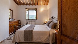 A bedroom with a wooden ceiling, a bed with a headboard, a dresser, a window with a view, and a nightstand with a lamp. - Apartment "Pugnano Alto - Tartufo" with Shared Pool and Wi-Fi (lisciano niccone)