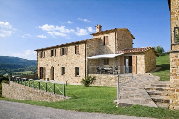 A stone building with a patio, outdoor seating, and a view of the countryside.
